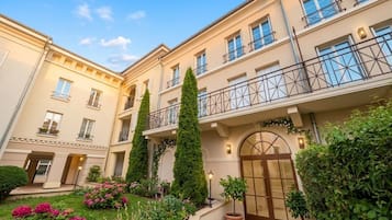 A multi-story hotel with a central courtyard, balconies, and a variety of plants.
