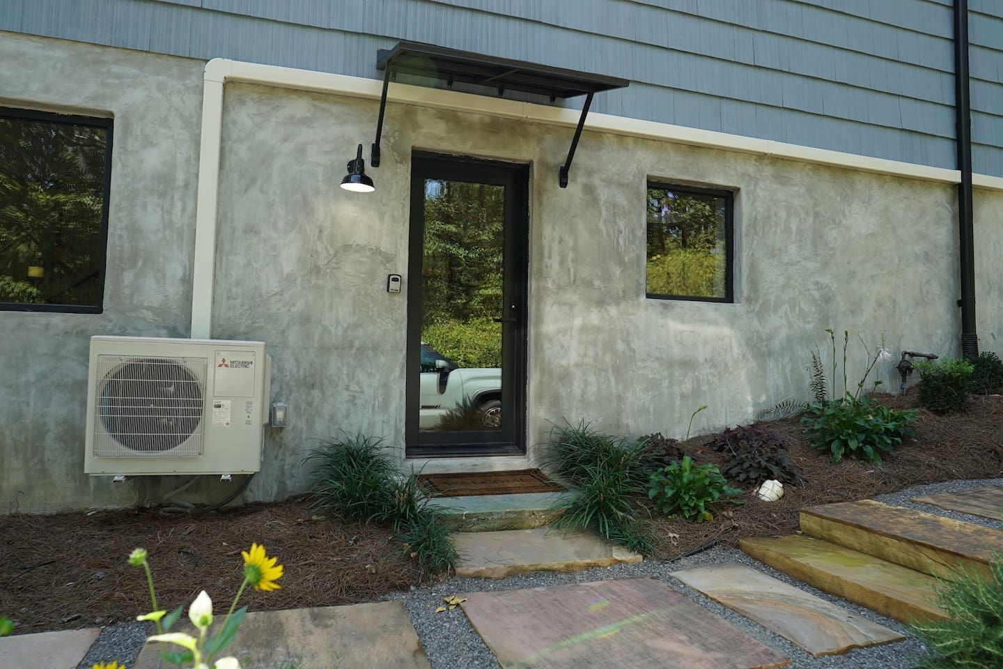 A modern house with a concrete exterior, a black door, and an air conditioning unit.