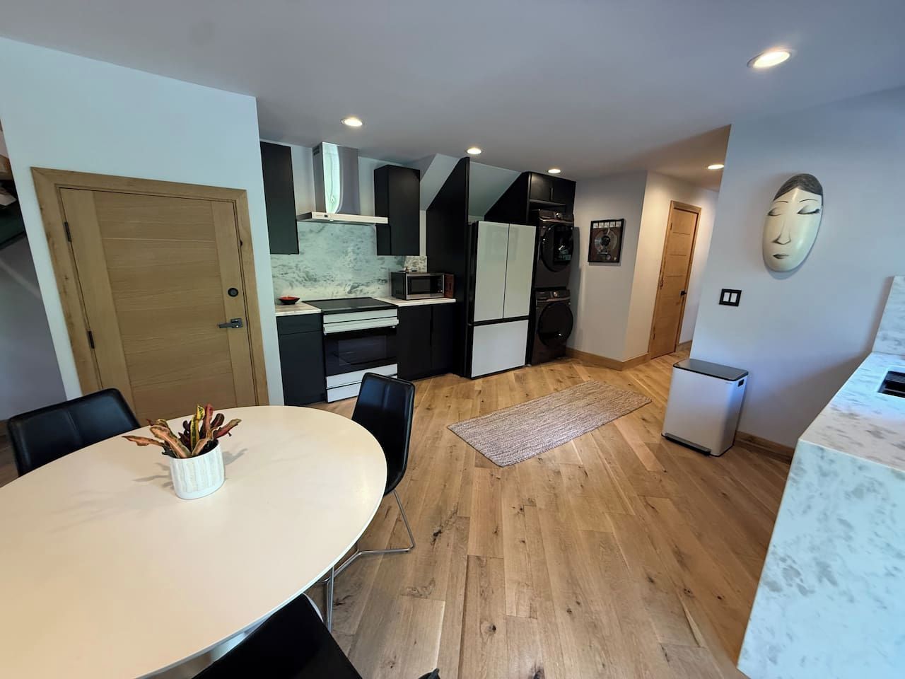Una cocina compacta con electrodomésticos modernos, una mesa de comedor con sillas y piso de madera.
