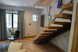 A modern interior with a wooden staircase, a black chair, a potted plant, and a small window. - The Oakley Art House (Chattanooga)