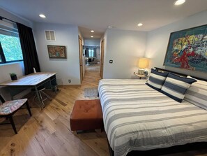 Ein Schlafzimmer mit Bett, Schreibtisch und Stuhl. Ein Fenster mit Vorhängen, ein Bild an der Wand und eine Lampe auf dem Nachttisch.