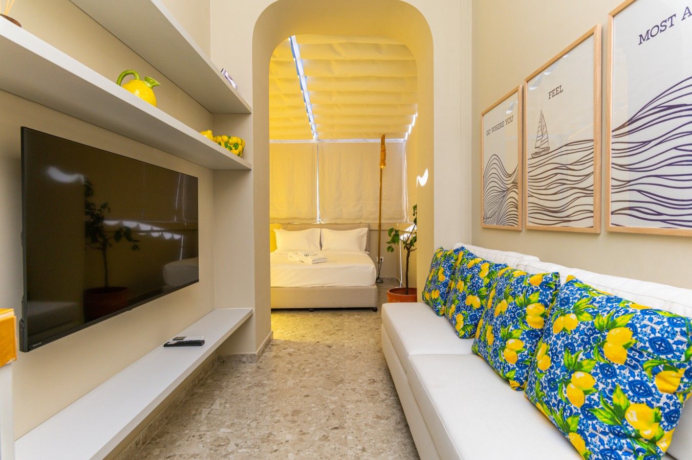 A hotel room with a TV, a bed, a sofa, and artwork on the walls.