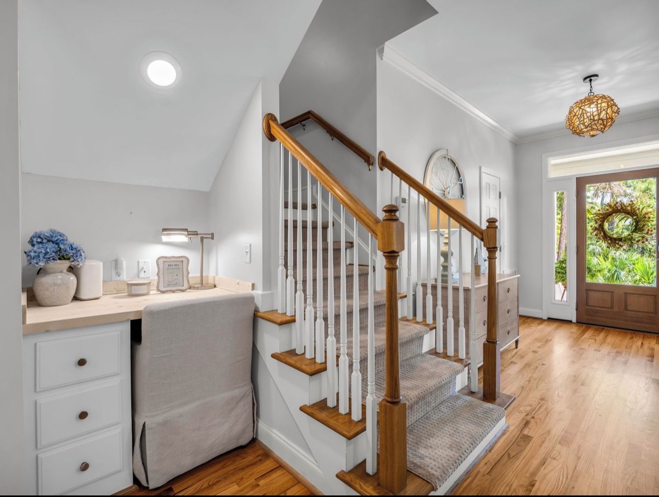 A modern kitchen with a wooden staircase, white cabinetry, and a view of the outdoors.