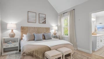 A bedroom with a bed, bedside tables, a nightstand, a window with curtains, and a view of a bathroom.