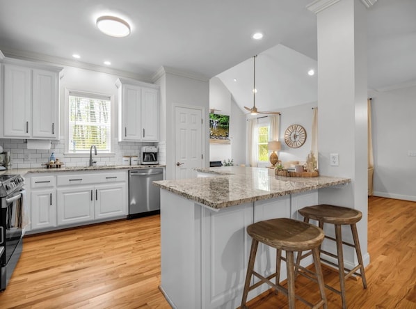 A modern kitchen with white cabinetry, a granite countertop island with stools, and a ceiling fan.