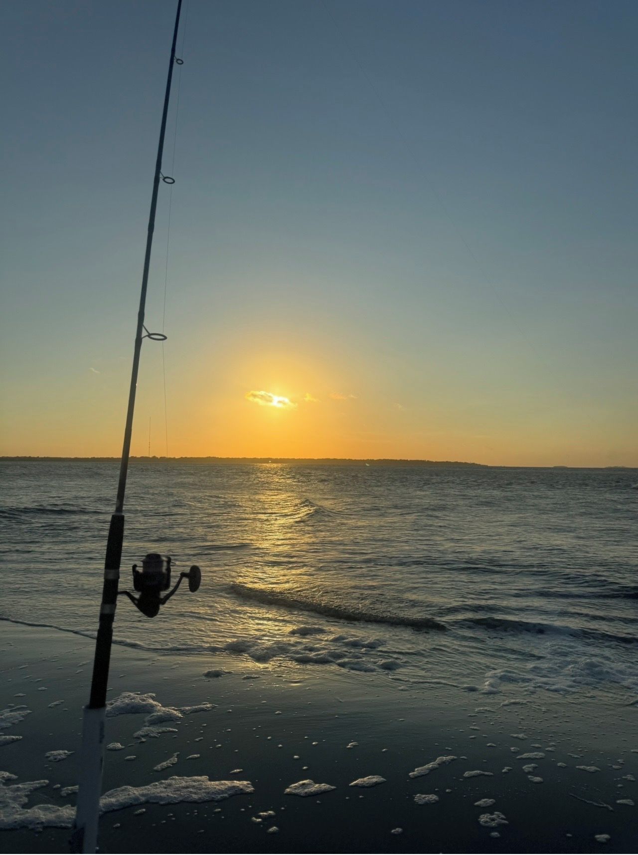 A fishing rod with a reel, positioned over a body of water during sunset.