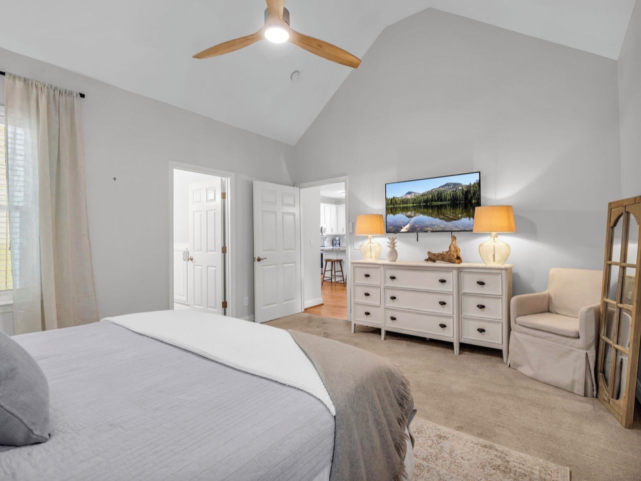 A bedroom with a bed, a dresser, a chair, a television, and a ceiling fan.