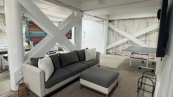 A covered outdoor seating area with a grey sectional sofa, a small ottoman, and a patterned rug.