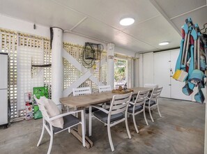 A dining area with a wooden table and white chairs, a white ceiling, and a white wall with a window.