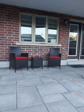 A patio with two wicker chairs and a small table, a brick wall, and a sliding glass door. - Luxury Walkout Basement Suite near Lake and Conservation Park (Pickering)