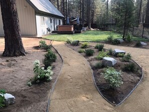A landscaped backyard with a curved pathway, a wooden deck, and a house. - Beautiful 5-bedroom chalet in serene South Lake Tahoe perfect for families (South Lake Tahoe)
