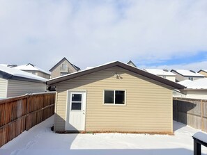 Une maison de plain-pied avec une porte et une fenêtre blanches, entourée d’une clôture en bois, située dans un paysage enneigé.