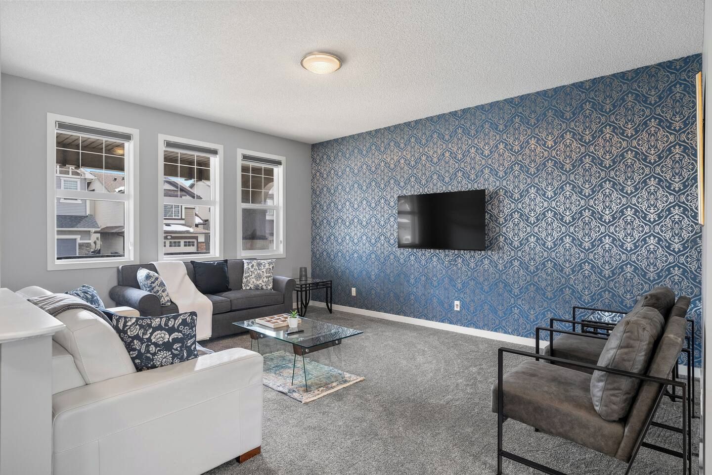A living room with a grey sofa, a white sofa, a coffee table, a patterned wall, and a mounted TV.