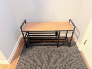 Une pièce d’angle avec un banc en bois adossé au mur, un tapis à motifs sur le sol et une porte blanche.