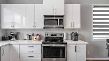 A modern kitchen with white cabinets, a stainless steel microwave, a stove, and a coffee maker.