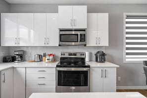 Une cuisine moderne avec des meubles blancs, un four à micro-ondes en acier inoxydable, une cuisinière et une machine à café.