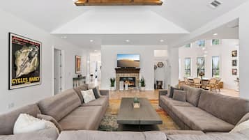 A spacious living room with a fireplace, two sofas, a coffee table, and a large TV screen.