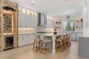 Een moderne keuken met witte kasten, een centraal eiland met zitplaatsen en een stenen muur.