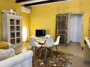 A dining area with a round table, white chairs, a television, and a cabinet with glass doors. - Villa with Outdoor Kitchen and Coastal Garden (Favignana)