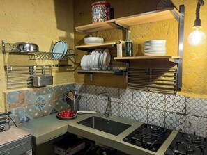 Una cocina con un lavamanos, estufa y estantes con platos y una botella.