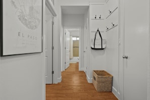 Un couloir avec un plancher en bois, des murs blancs et des portes. Un plan encadré est accroché au mur de gauche et un panier se trouve sur le mur de droite.