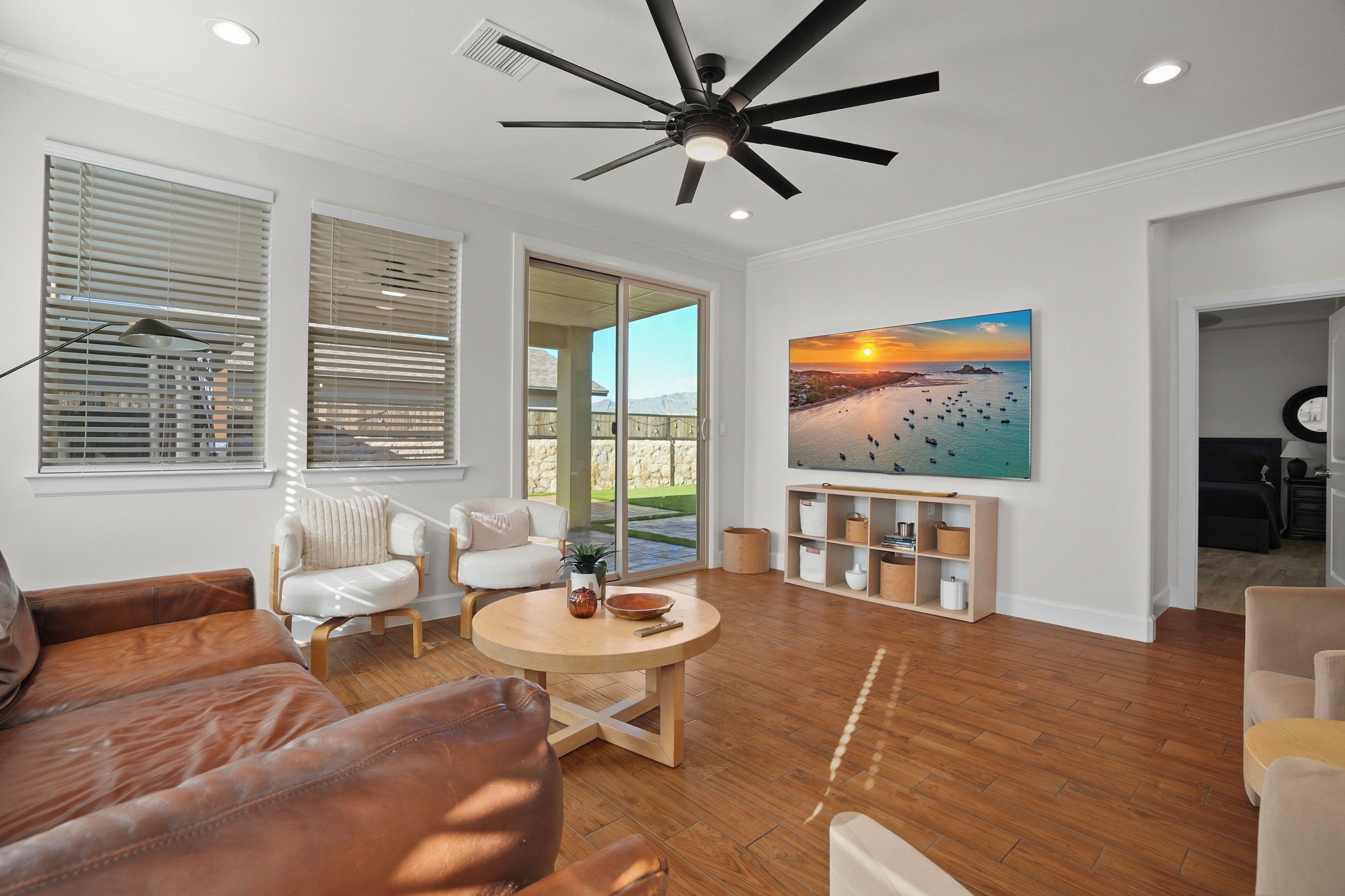A spacious living room with a large ceiling fan, a wooden floor, a sofa, a coffee table, and a painting of a sunset over a body of water.