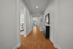 Un couloir doté d’un plancher en bois, de murs blancs et d’un meuble noir avec un miroir.