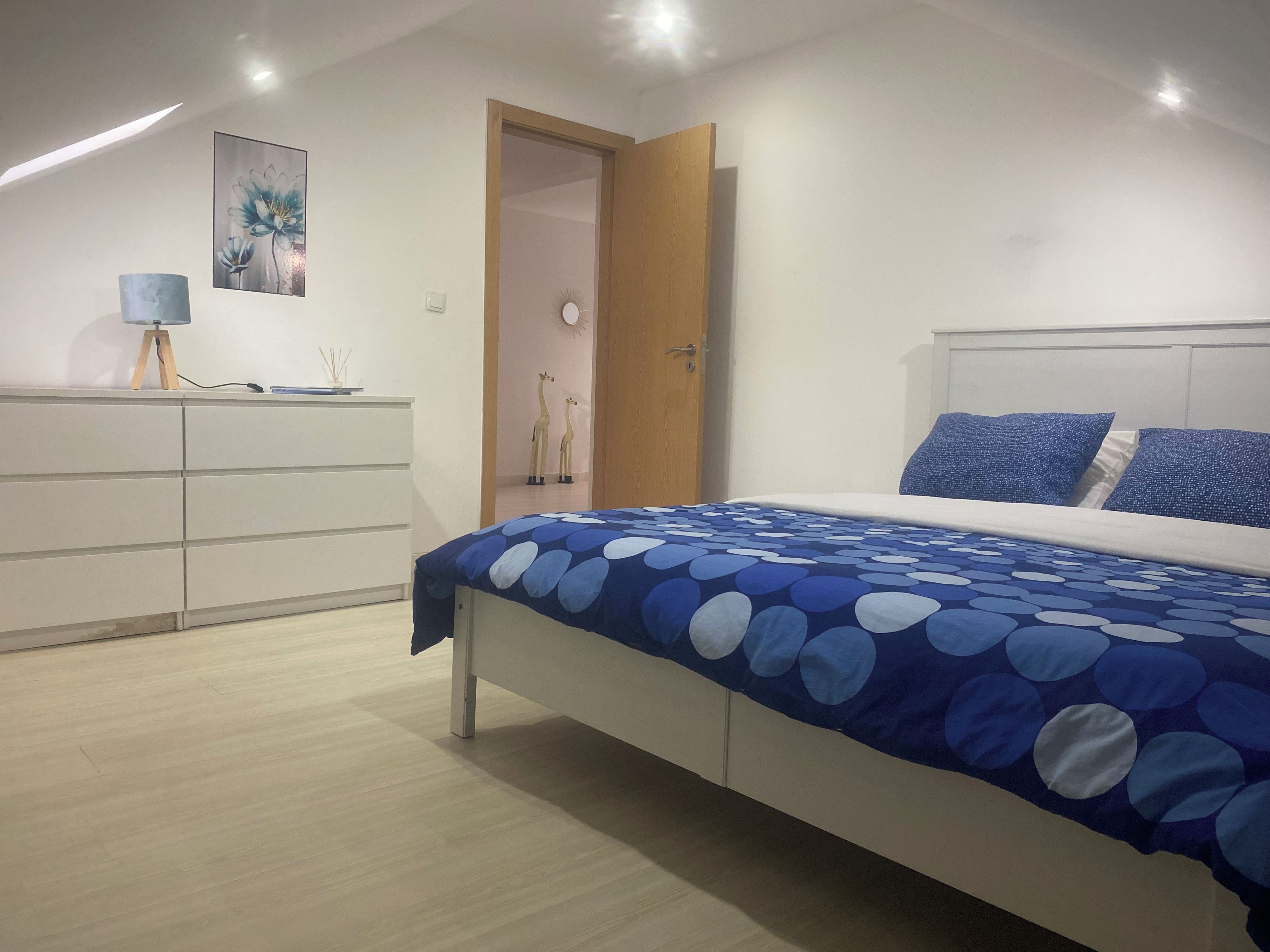 Une chambre à coucher avec un lit, une commode, une porte et une lampe fixée au mur.