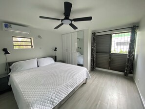 Un dormitorio con cama, ventilador de techo, ventana y puerta.