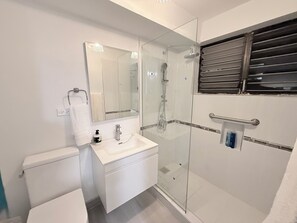Un baño moderno con ducha de vidrio, lavamanos blanco y retrete.