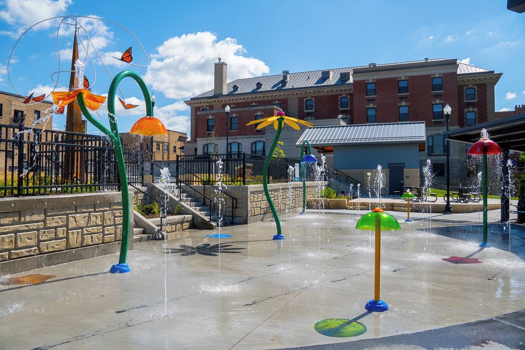 An outdoor water feature with multiple fountains and decorative elements, set against a backdrop of a brick building.