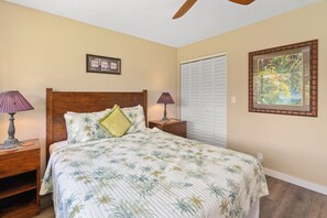 A bedroom with a bed, two nightstands, a ceiling fan, a framed picture, a closet, and a window. - Luxury 2-bedroom 2-bath condo in beautiful Princeville perfect for relaxing (Princeville)