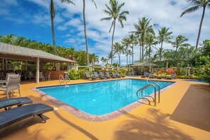 A swimming pool with lounge chairs and a covered seating area, surrounded by palm trees. - Luxury 2-bedroom 2-bath condo in beautiful Princeville perfect for relaxing (Princeville)