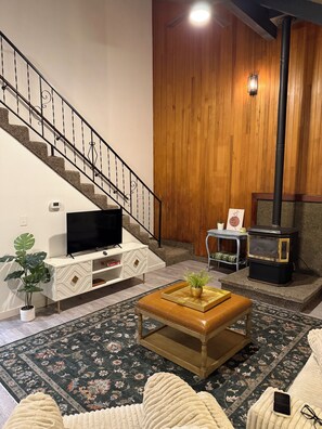 Un salon avec un escalier, un téléviseur, une cheminée et une table basse.