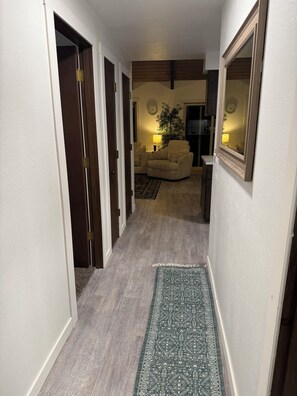 Un couloir recouvert d’une moquette mène à un salon où se trouvent un canapé et une lampe.