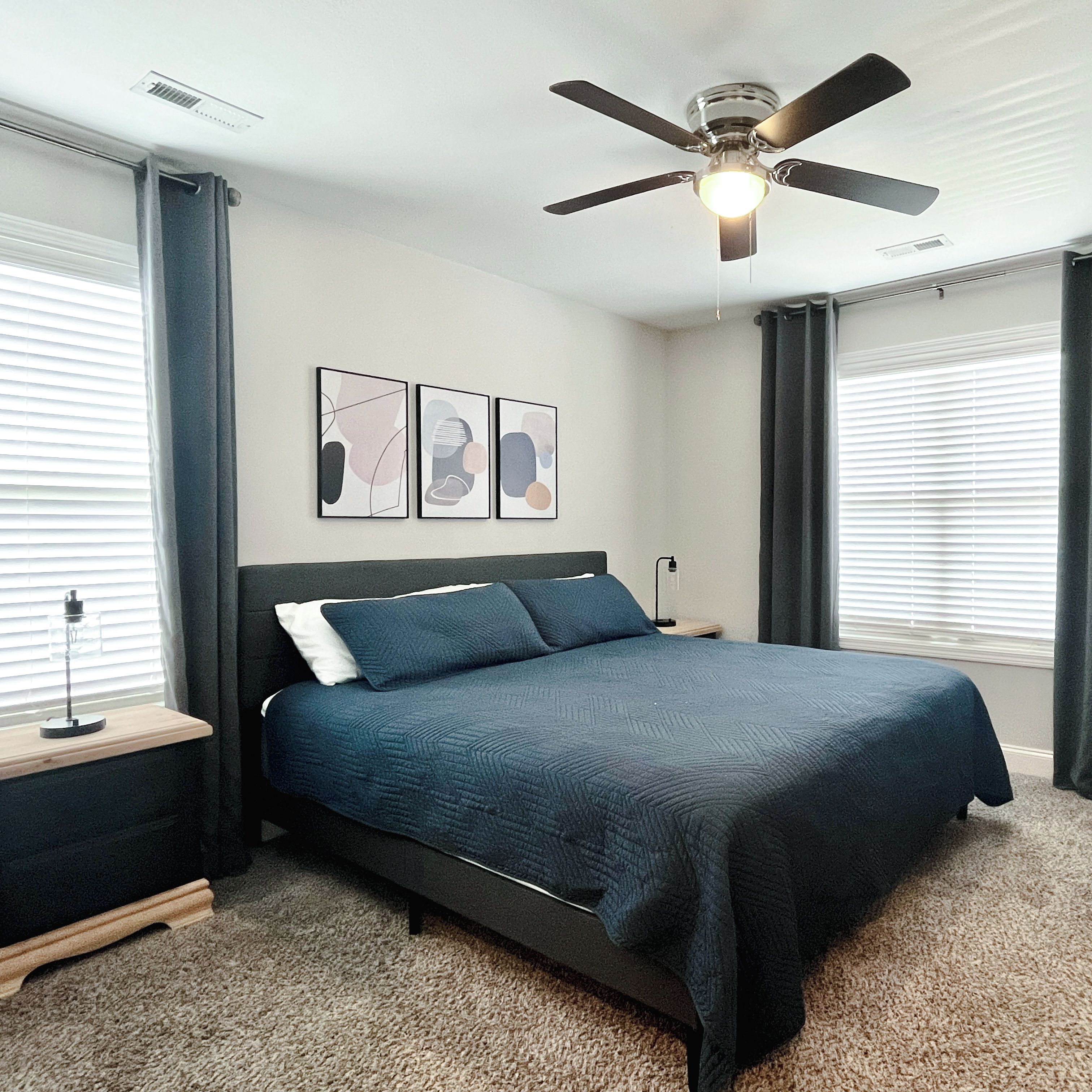A bedroom with a bed, a ceiling fan, and three wall-mounted pictures.