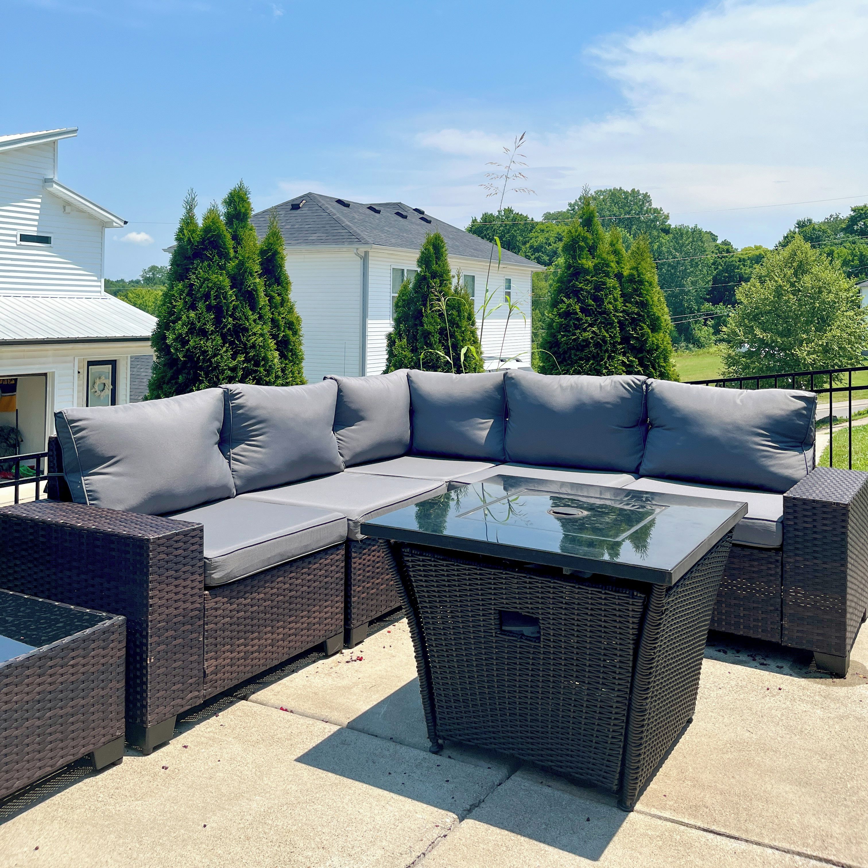A sectional sofa with cushions and a glass-top coffee table on an outdoor patio.