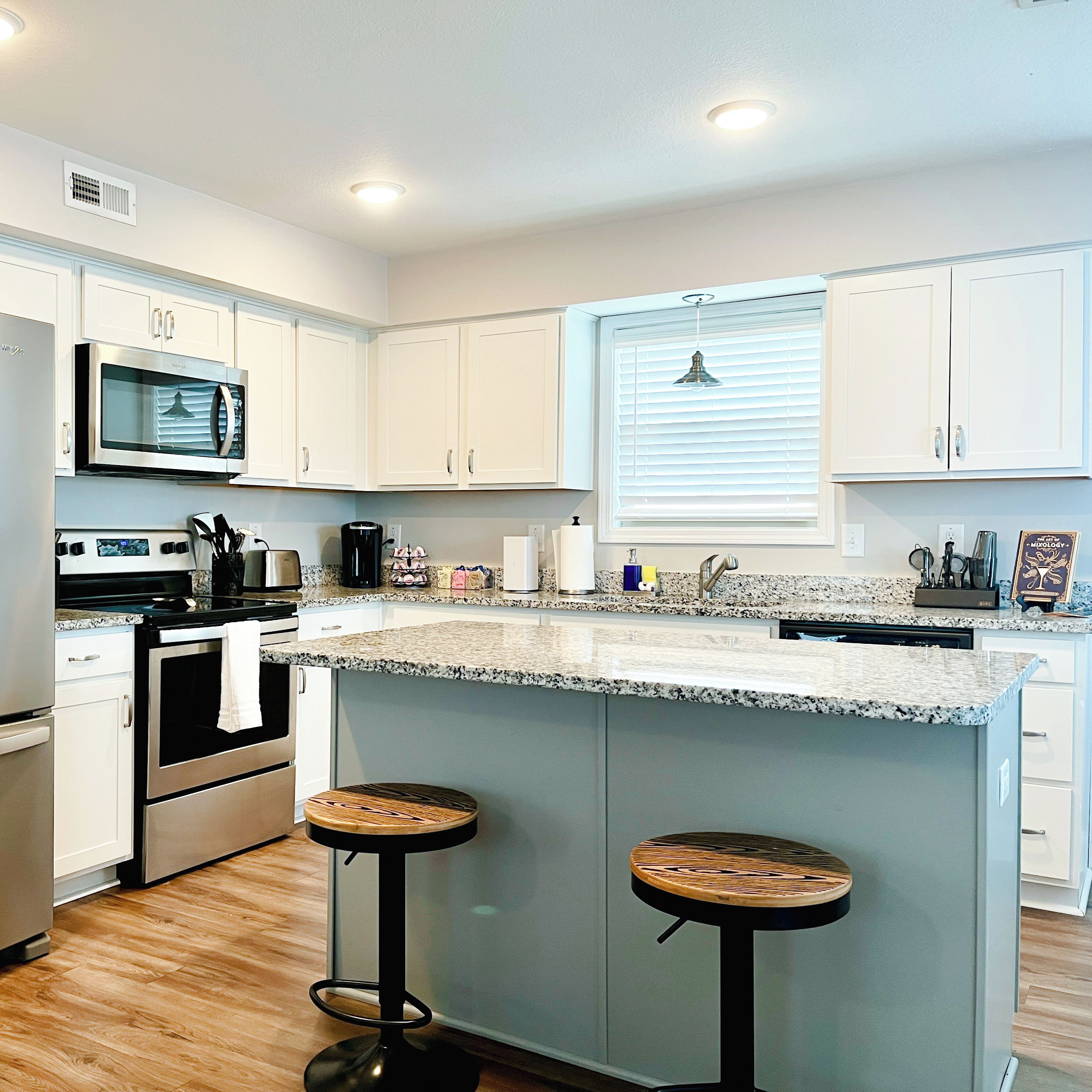 A modern kitchen with white cabinets, a granite countertop, stainless steel appliances, and two stools.