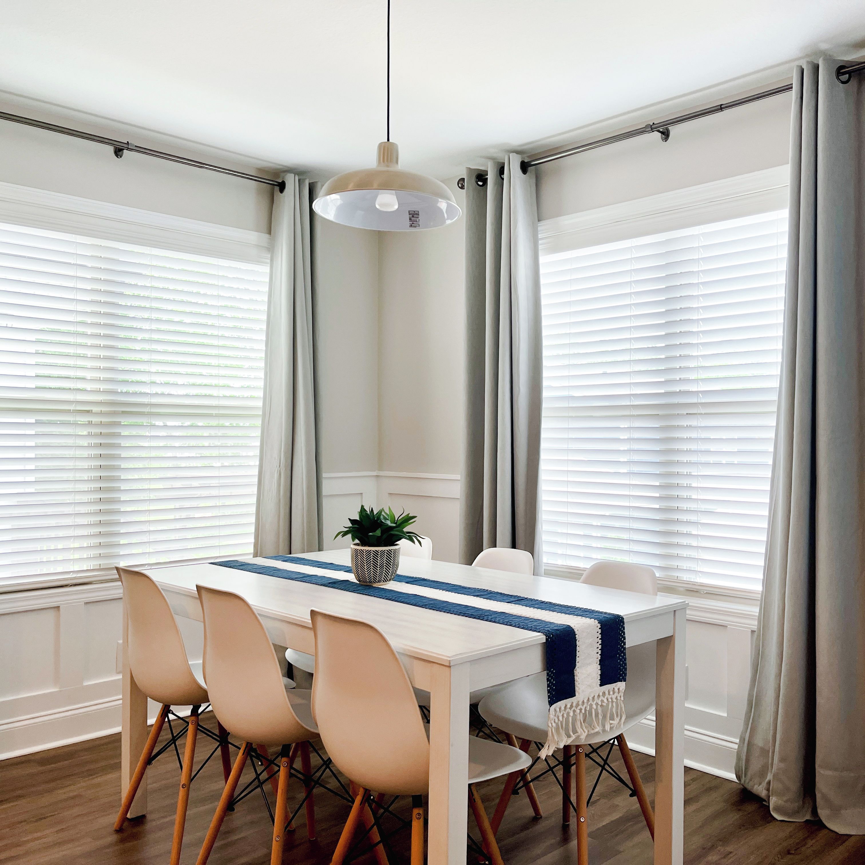 A dining area with a table, chairs, a hanging light fixture, and a potted plant.