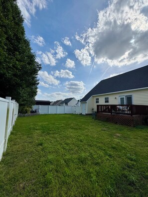 A residential backyard with a white fence, a lawn, and a house with a dark roof. - >The Pacific Home< (Winterville)