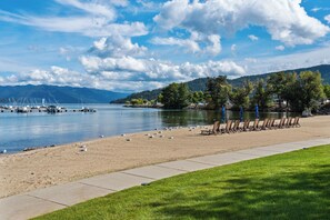A lakeside beach with a row of beach chairs and a grassy area. - Lakefront Luxury Downtown w/ Pool, Hot Tub & Dock (Sandpoint)