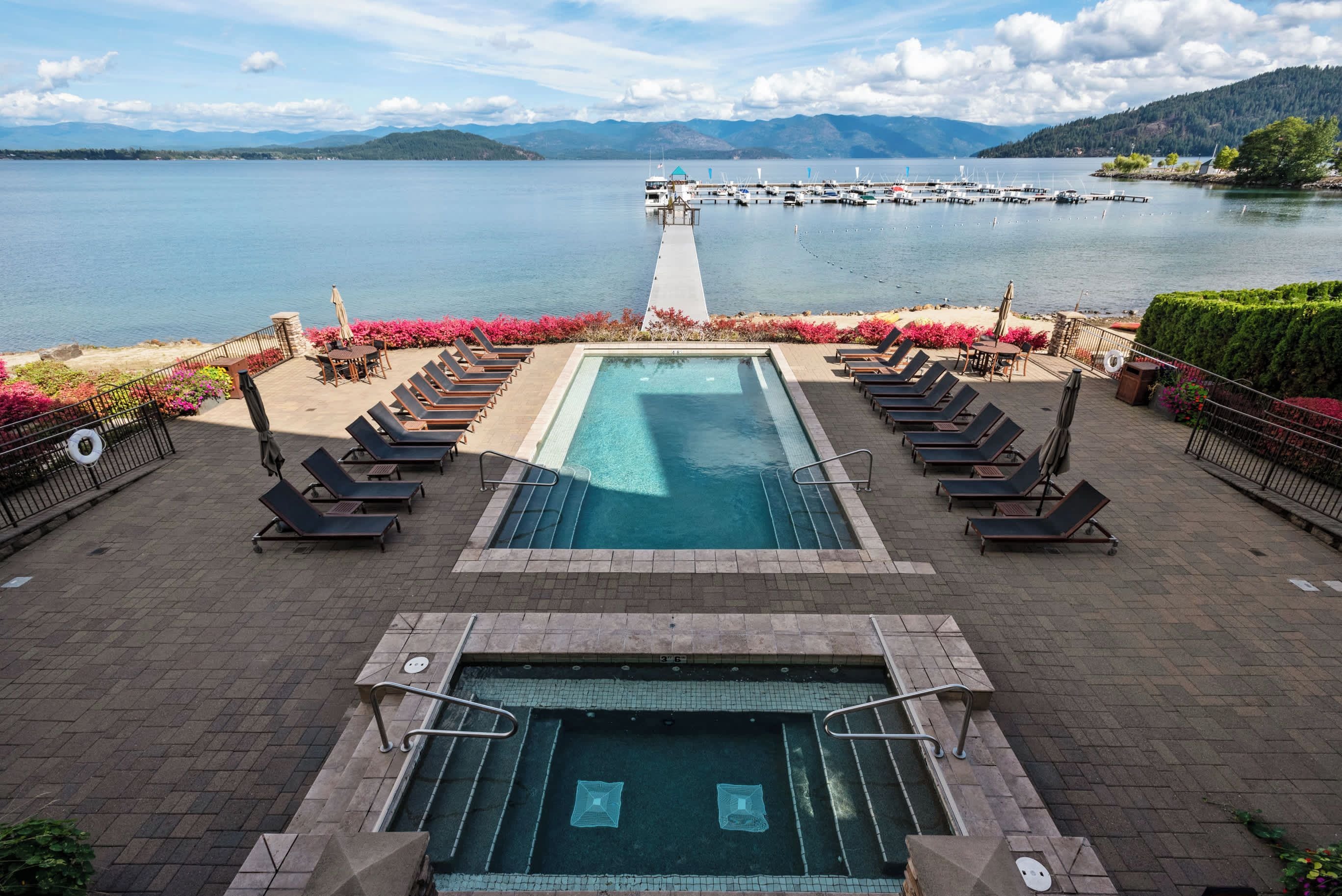 A pool area with lounge chairs and a view of a lake with boats.