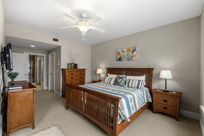 Een slaapkamer met een houten bed, nachtkastjes, een bureau en een plafondventilator.
