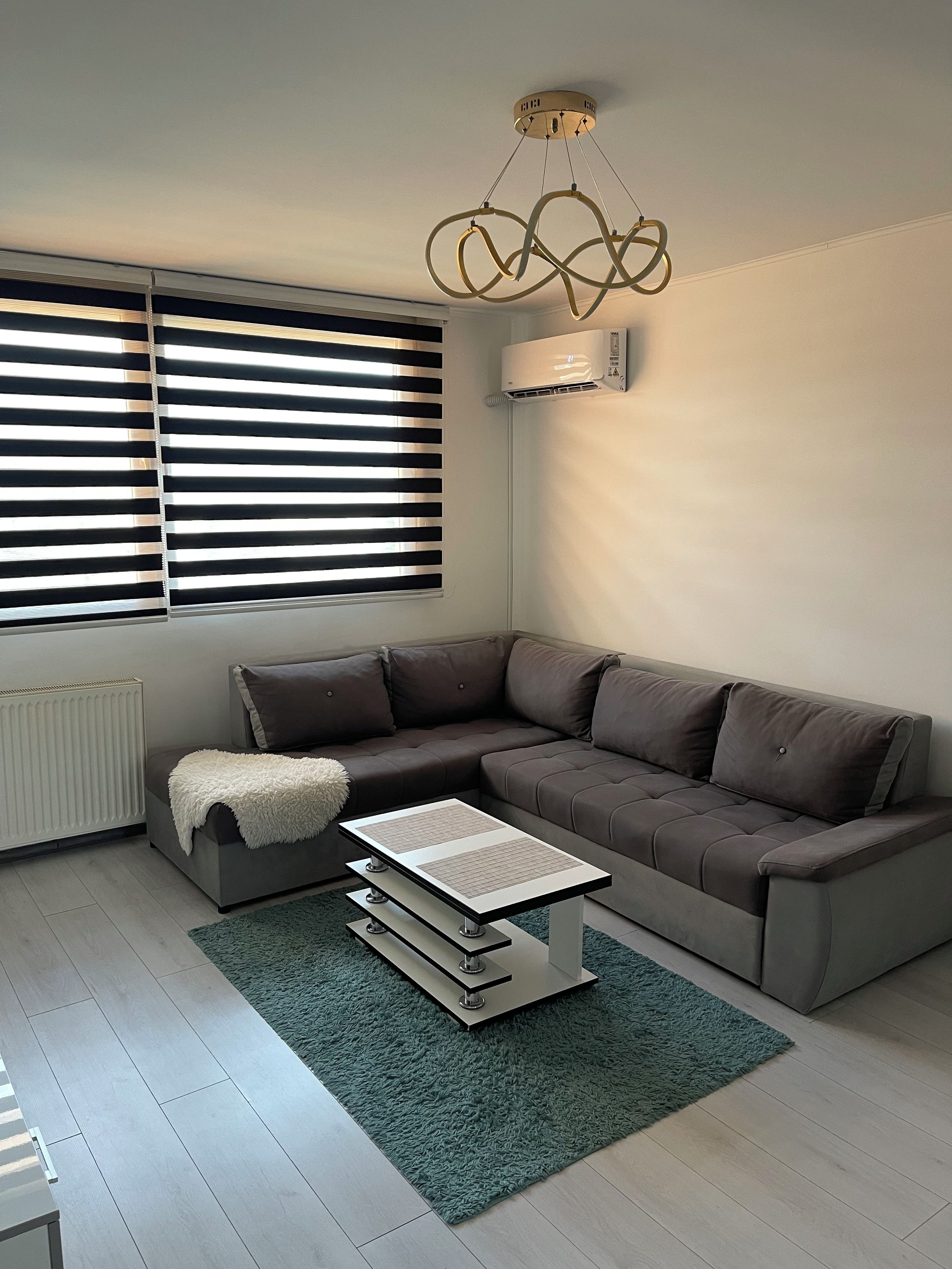Una sala de estar moderna con un sofá seccional, una mesa de centro, un radiador y una ventana con persianas.