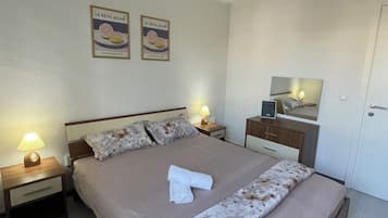 Una cama bien tendida con una colcha estampada, dos lámparas de noche, una mesita de noche, un aparador y un espejo en la pared.