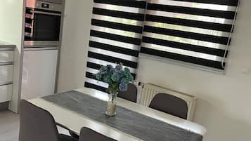 A dining area with a table, chairs, a vase with flowers, and a kitchen with appliances.