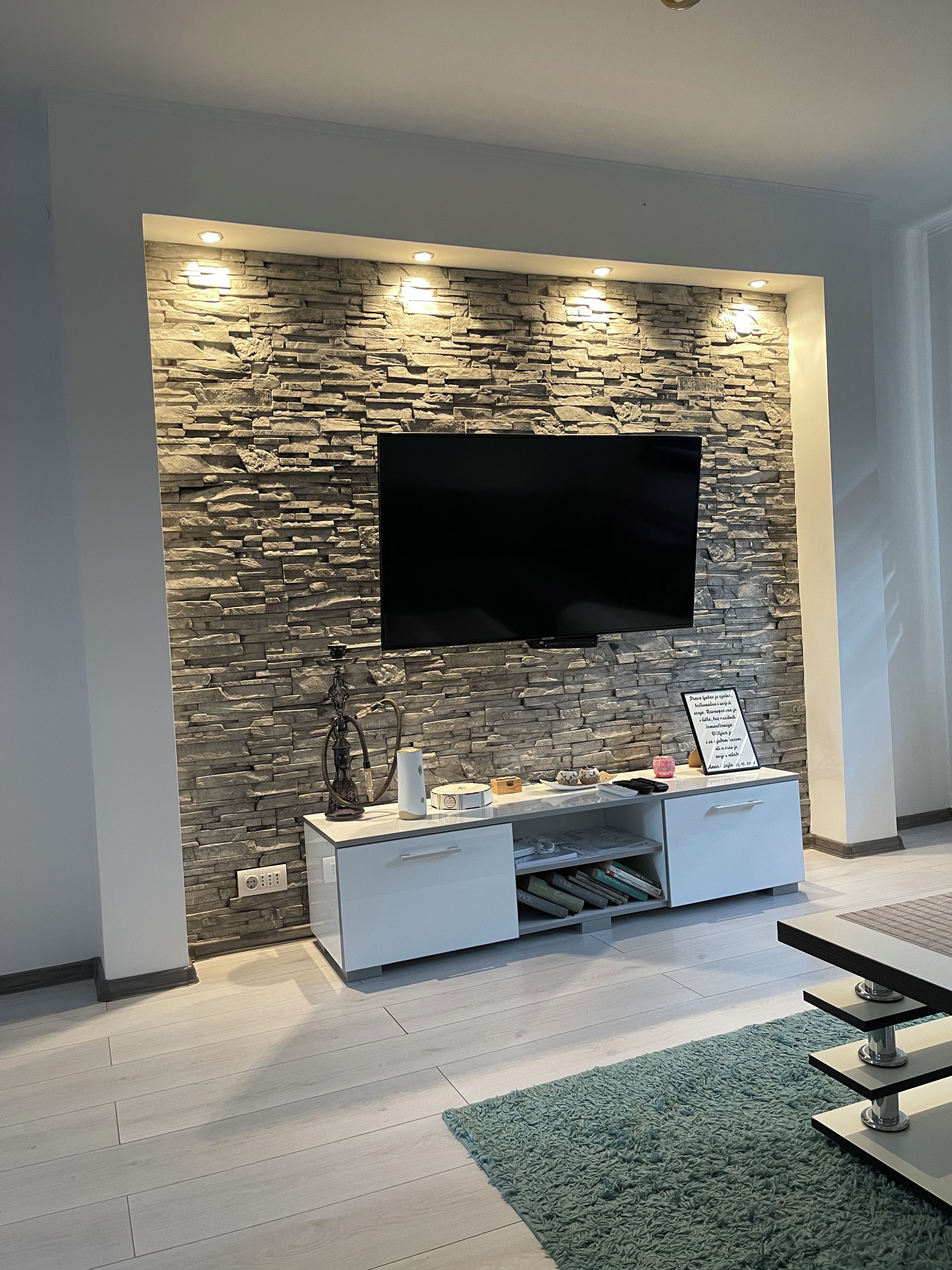 Ein modernes Wohnzimmer mit einer Steinwand, einem Flachbildfernseher, einer weißen Unterhaltungseinheit und einem grünen Teppich.