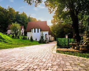 A cobblestone street leading to a white building with a red roof, surrounded by greenery and trees.