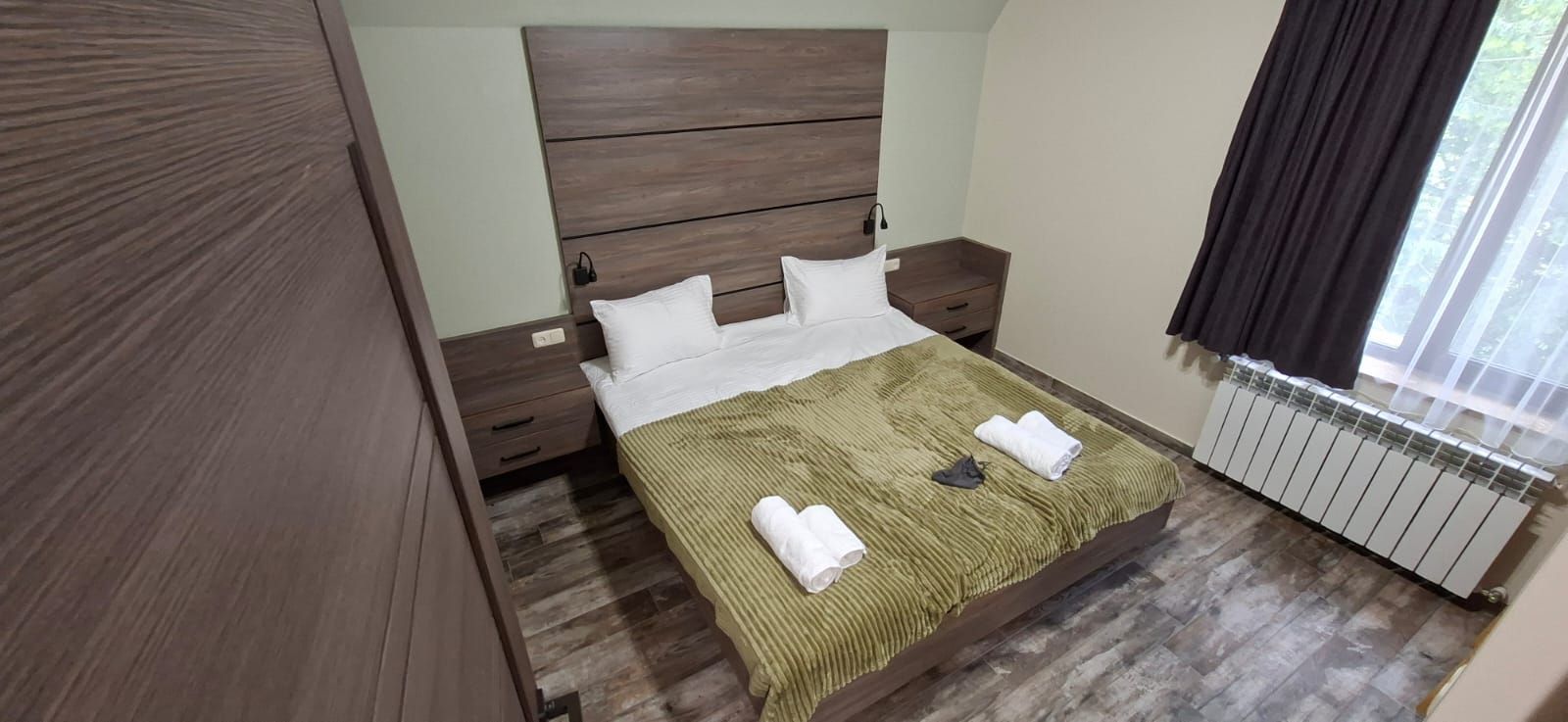 Una camera da letto con una testiera in legno, un letto con lenzuola bianche, una coperta a righe verdi e un termosifone.