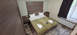 A bedroom with a wooden headboard, a bed with white linens, a green striped blanket, and a radiator.